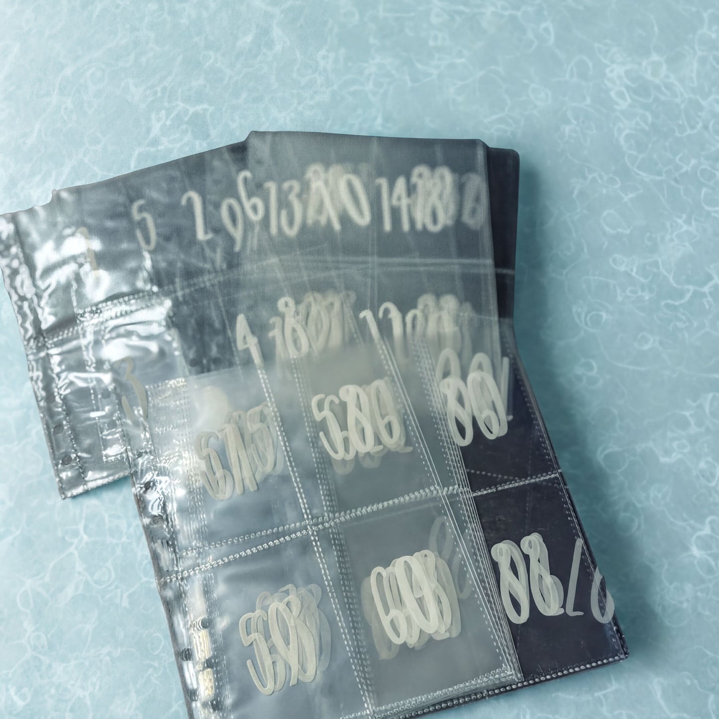 a collection of transparent plastic sleeves or cases, each containing a white text or number design. The text and numbers appear to be in a foreign language, and the image is not a typical photograph of a scene or object.