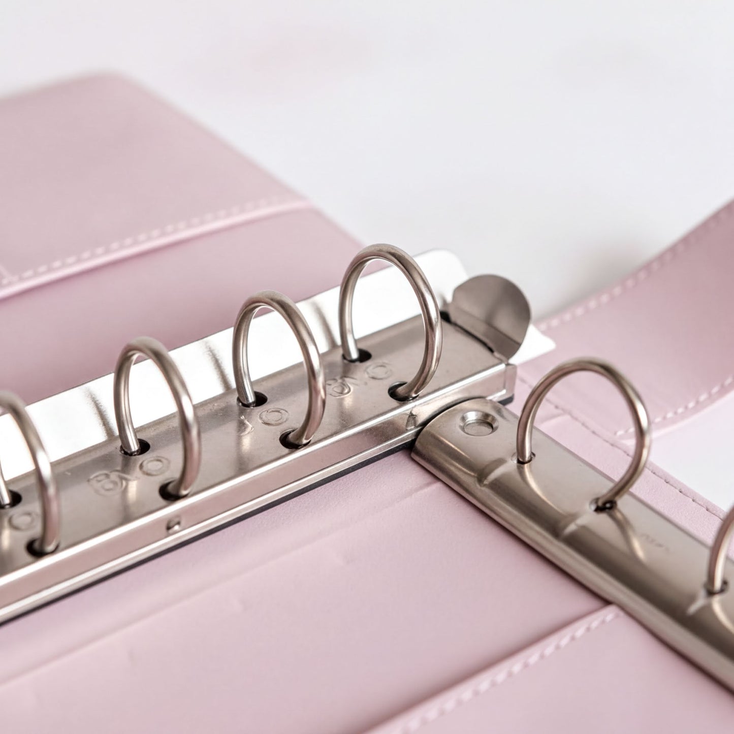 A close-up view of a metal ring mechanism on a pink leather-like surface.