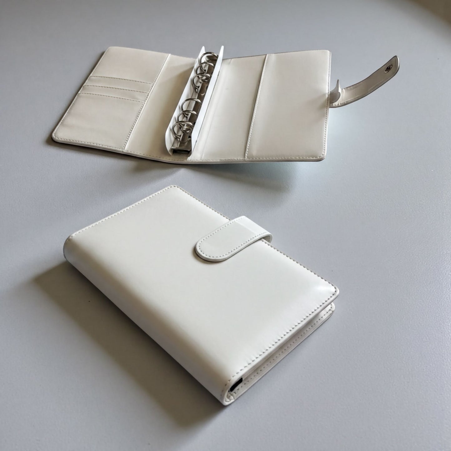 two white leather wallets or purses placed on a gray surface.