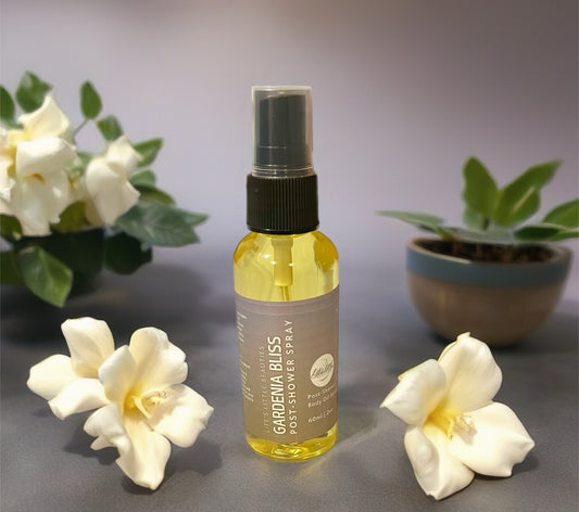 a bottle of Gardenia Bliss Post-Shower Spray surrounded by white flowers and leaves on a table.