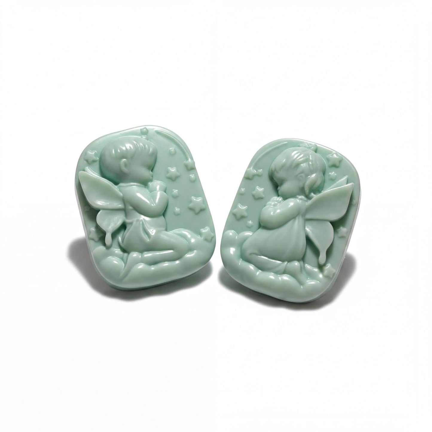 Two light green ceramic charms depicting cherubs or angels, each with wings and stars, are shown against a white background.