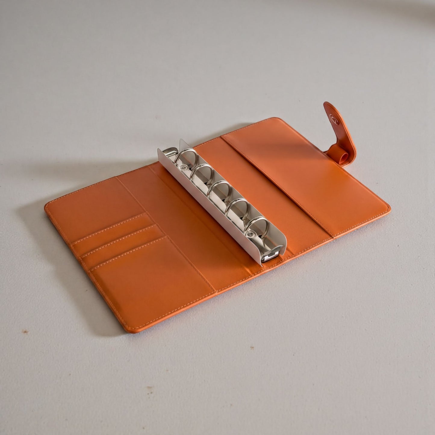 An orange leather binder with a metal ring holder is placed on a white surface.