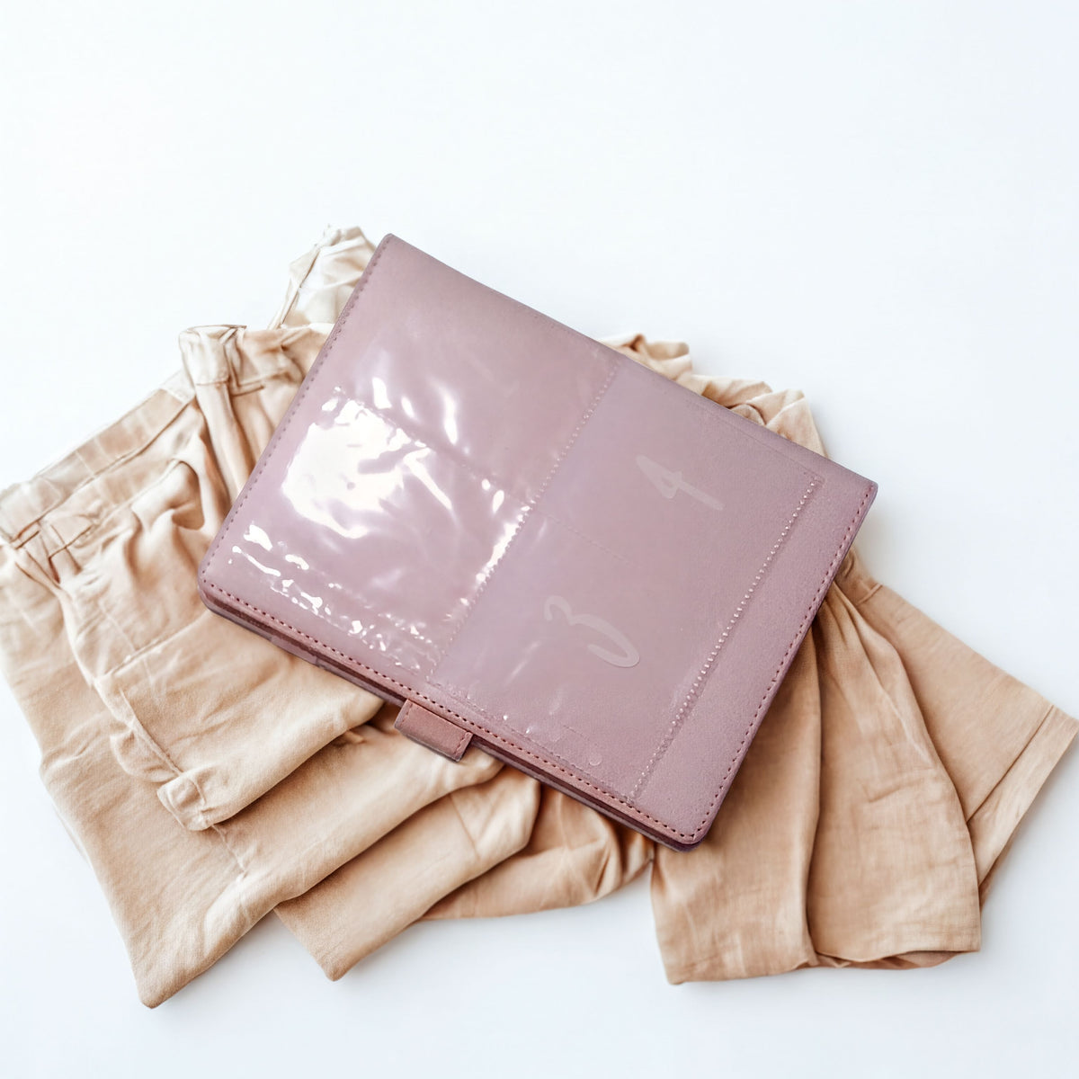Pink patent leather wallet on beige fabric, minimalist flat lay