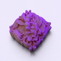 A square-shaped, purple soap with an intricate floral design on it.