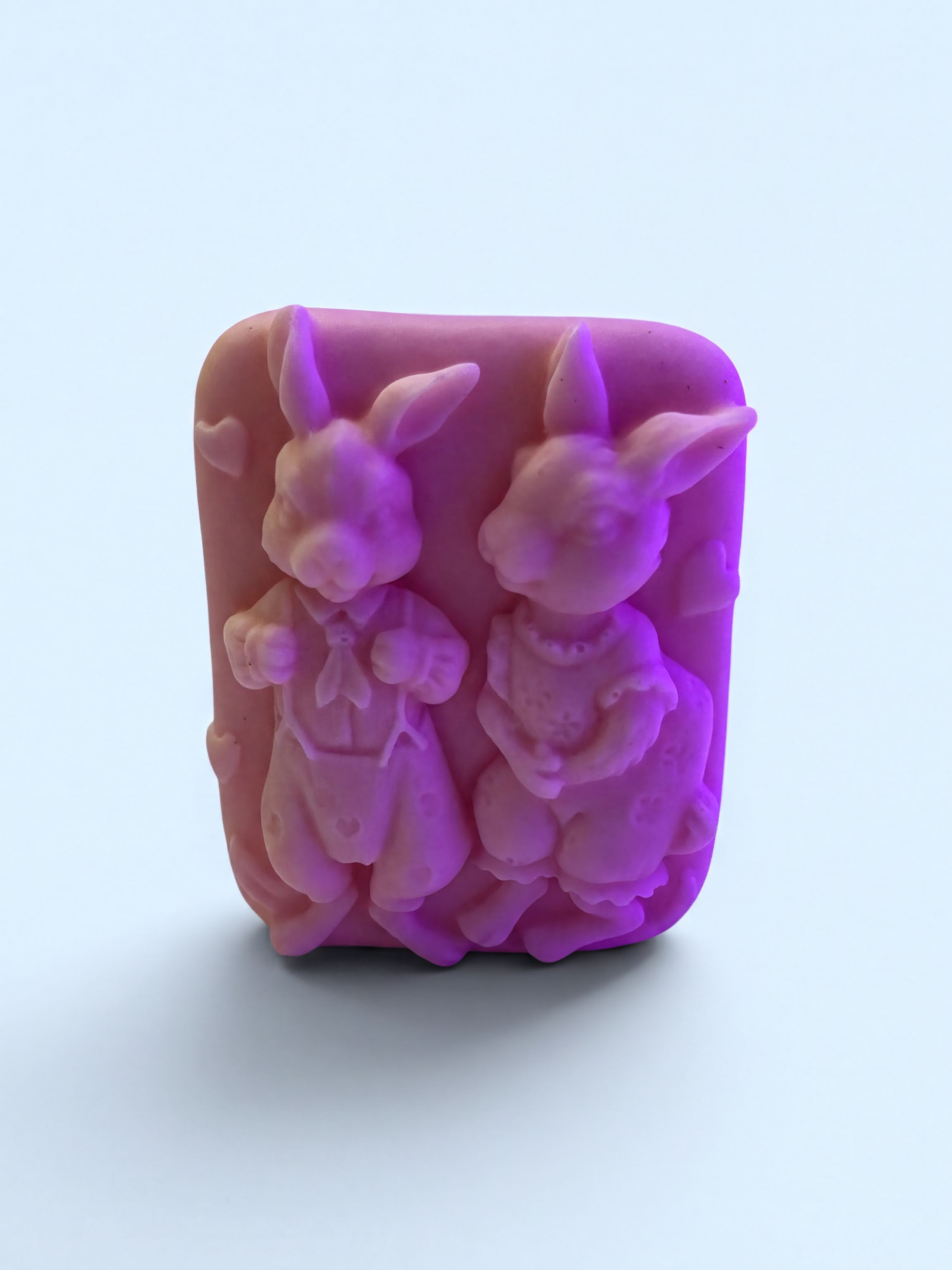 A pink soap bar with two cute rabbit-like figures on it.