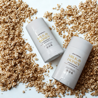 Two white deodorant sticks with the text "OATMEAL MILK & HONEY DEODORANT" are placed on a white surface, surrounded by scattered oat flakes.