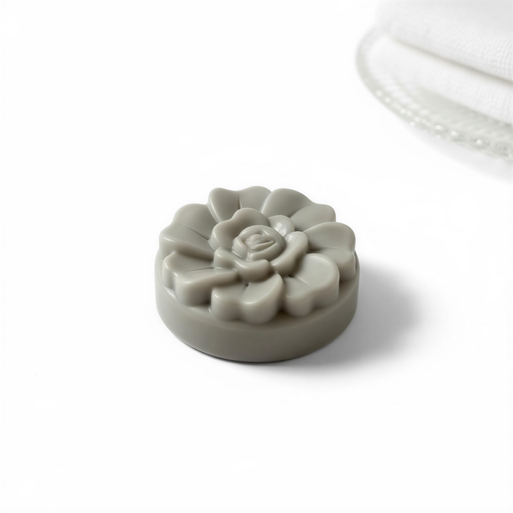 A gray, round soap with a flower-shaped design sits on a white surface.