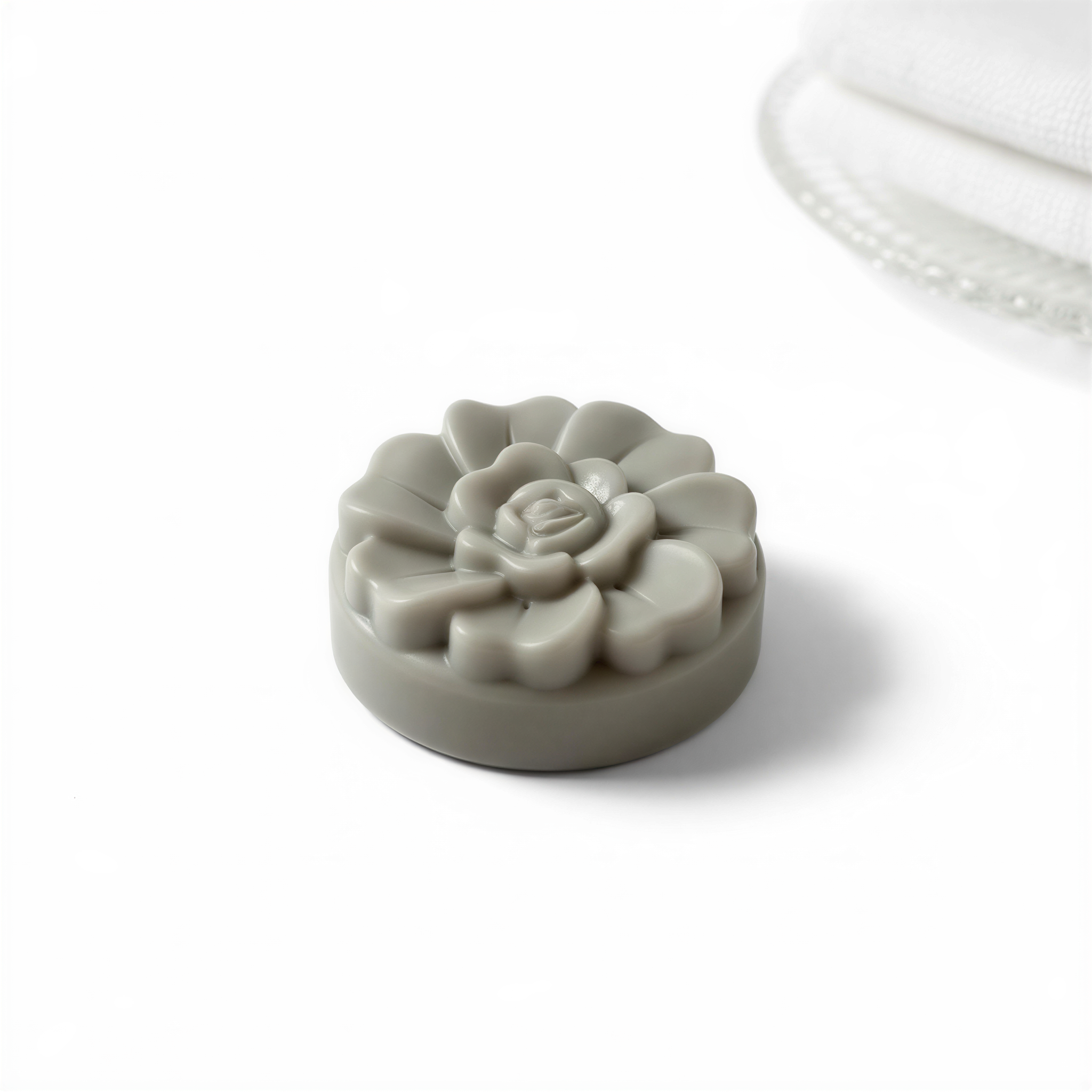A gray, round soap with a flower-shaped design sits on a white surface.