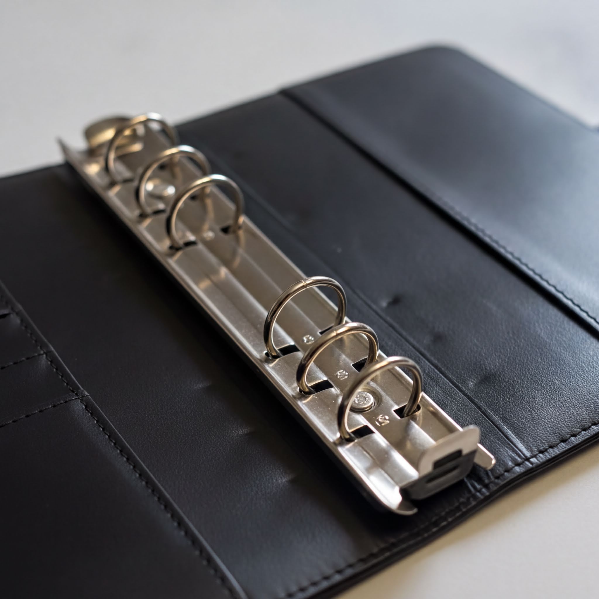 A black leather binder with a metal ring mechanism, which appears to be a page protector or cover for a notebook or binder.