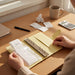 A person is sitting at a desk, looking at a yellow binder with a receipt inside, surrounded by various office supplies and a calculator.