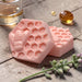 two pink honeycomb-shaped bars, a glass of liquid, and some small objects on a wooden surface.