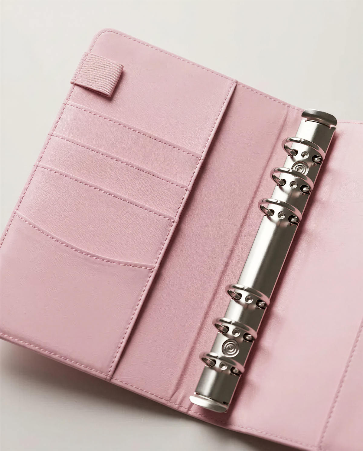 A pink leather-like notebook or planner with multiple pockets and rings, suggesting it is designed for organization and storage purposes.