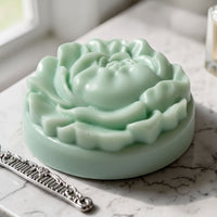 A round, green soap with a flower-shaped design sits on a marble countertop next to a silver comb.