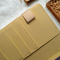 A close-up view of a beige leather wallet or card holder with a zipper closure and a small tag attached to it.