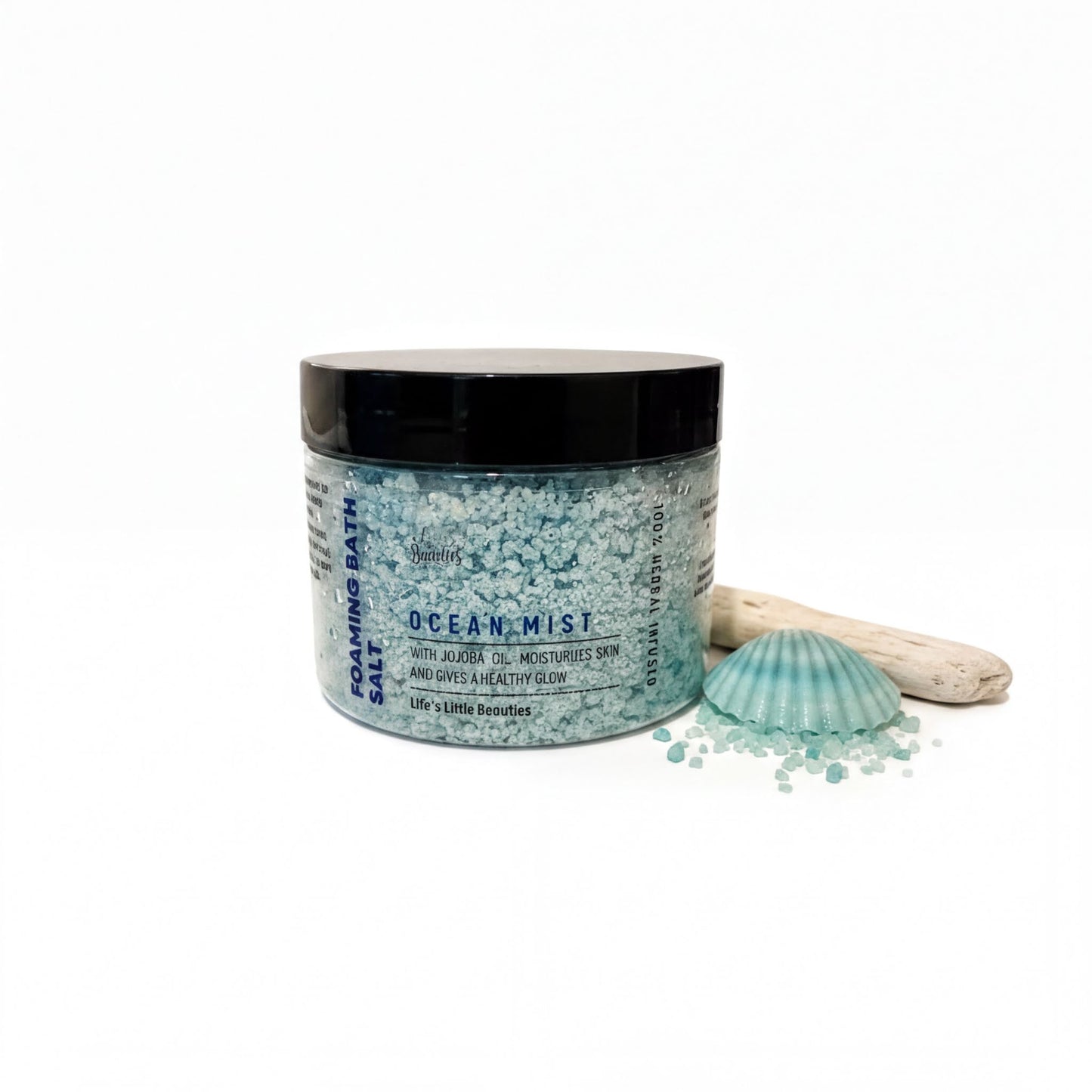 a jar of Ocean Mist salt bath with a black lid, surrounded by sea glass and a seashell.