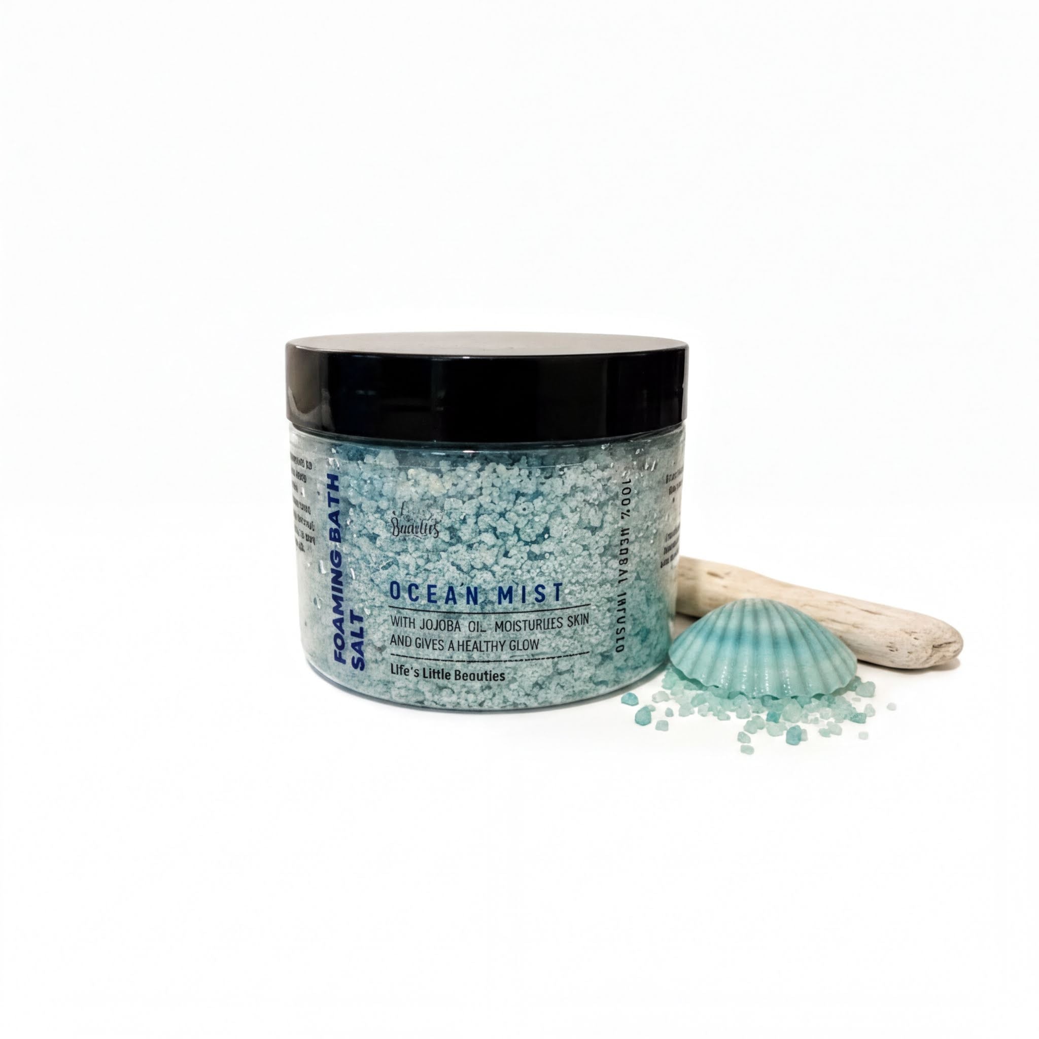 a jar of Ocean Mist salt bath with a black lid, surrounded by sea glass and a seashell.