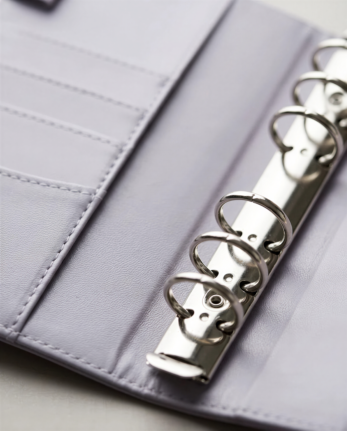 A close-up view of a silver metal ring on a light purple leather-like material, with the ring's teeth visible.