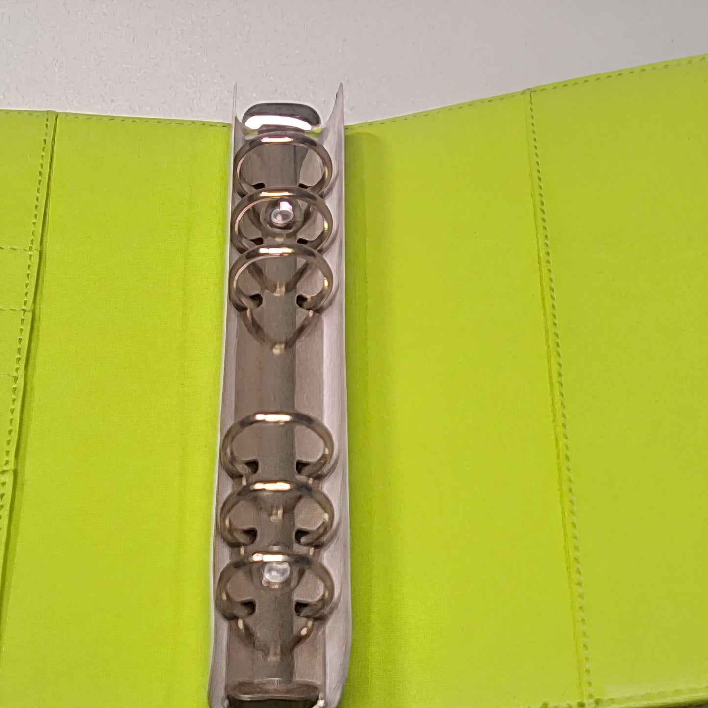 a silver metal ring with a white handle, placed inside a bright green folder or binder.