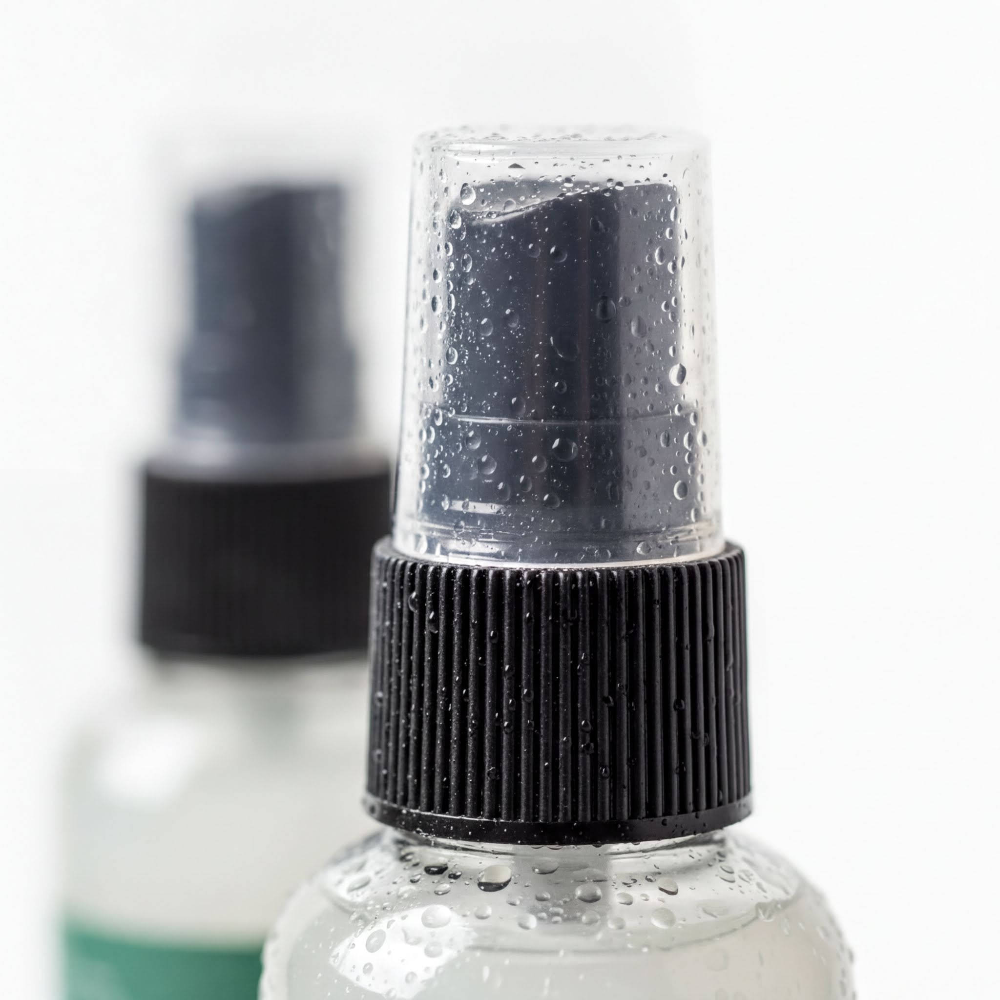 A close-up image of a spray bottle with a black cap and a clear plastic nozzle, with water droplets on the cap and nozzle.
