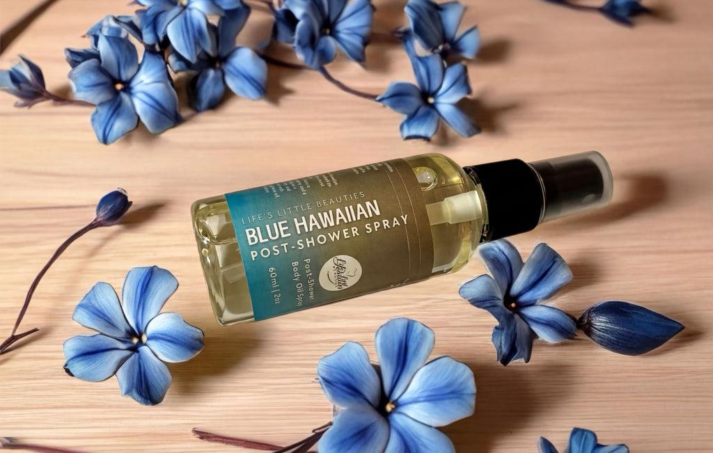 A bottle of "Life's Little Beauty" Blue Hawaiian Post-Shower Spray" surrounded by blue flowers on a wooden surface.