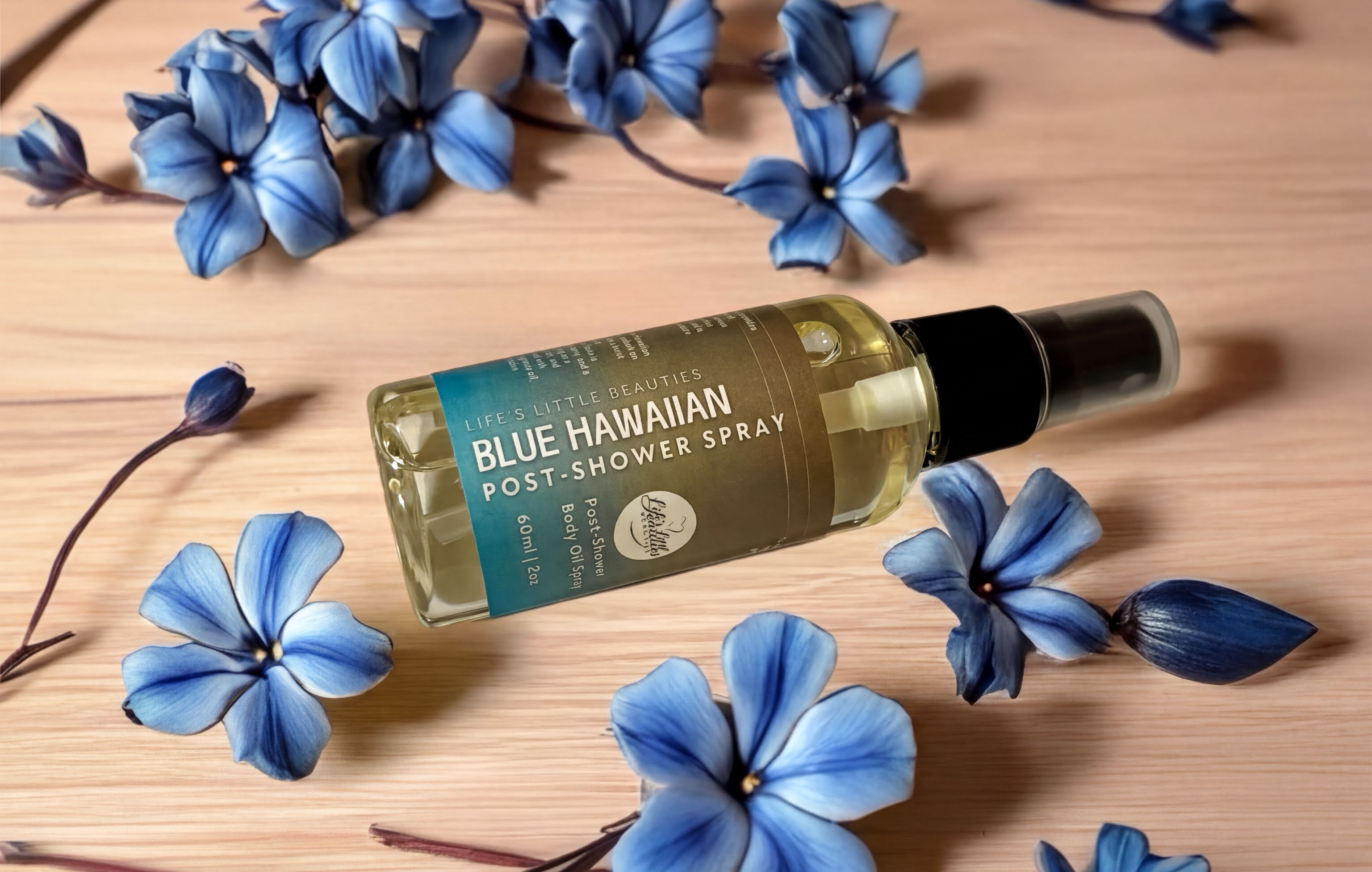 A bottle of "Life's Little Beauty" Blue Hawaiian Post-Shower Spray" surrounded by blue flowers on a wooden surface.
