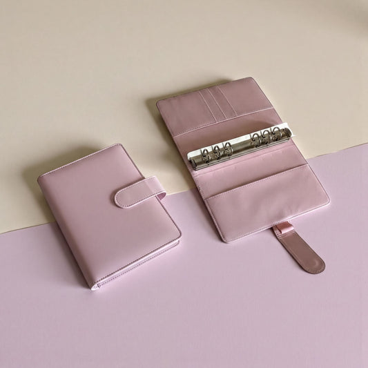 A pink notebook, a mug, and a laptop are arranged on a desk near a window, creating a cozy and organized workspace.