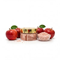 a jar of apple cider vinegar with a gold lid, surrounded by three apples and a small glass bowl filled with pink salt.