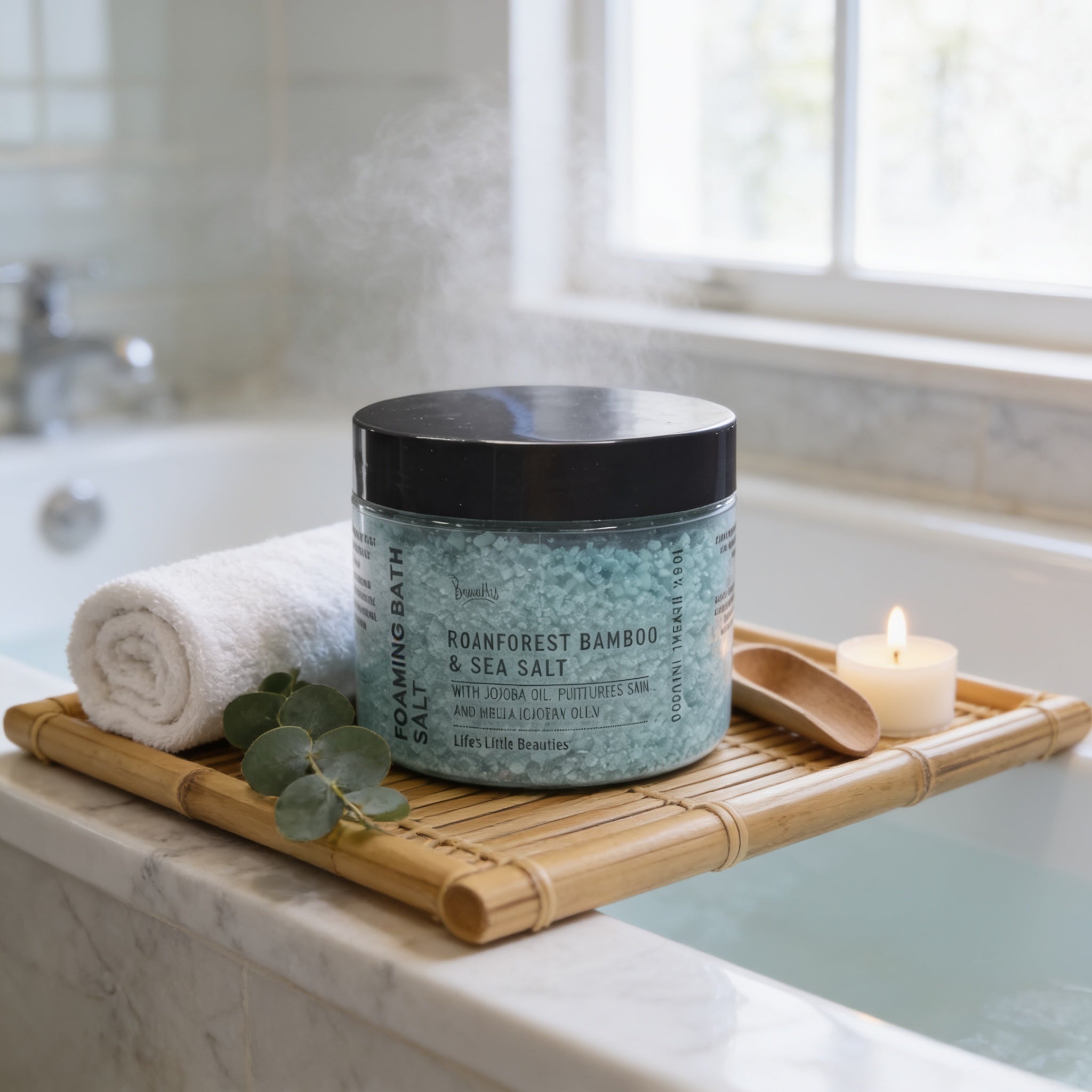 A jar of Roanforest Bamboo & Sea Salt Soaking Bath Salt is placed on a bamboo tray, with a lit candle and a rolled white towel nearby, in a bathroom setting.
