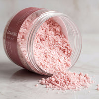 A jar of pink bath salt is spilling its contents onto a marble surface, creating a pink powdery substance.