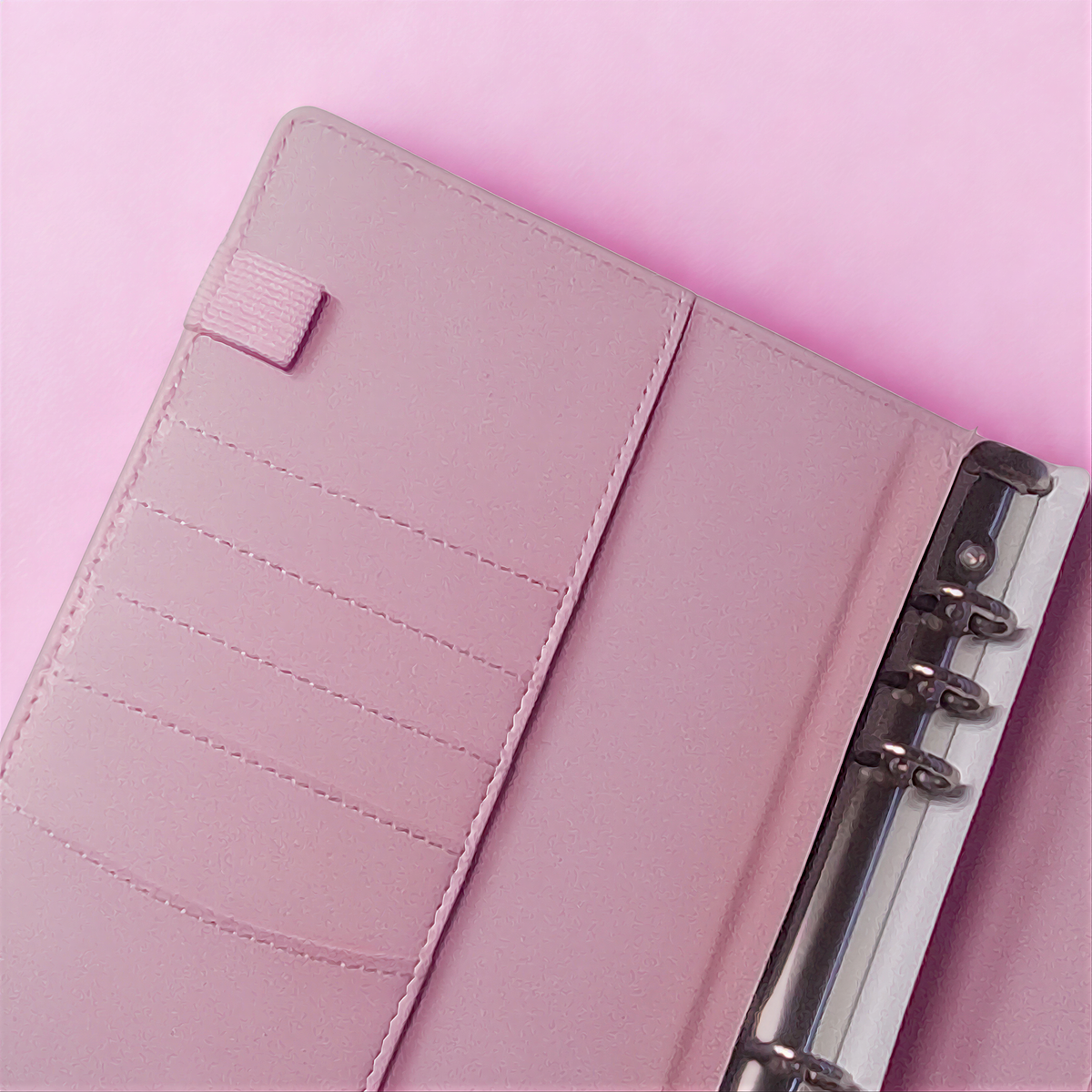 Pink leather notebook with card slots and metal binding on soft pink background