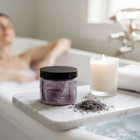 A woman relaxing in a bathtub, with a jar of lavender-scented bath salt and a lit candle nearby.