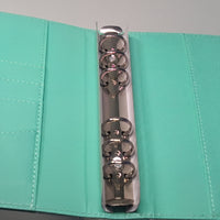 A silver metal binder ring is shown in an open turquoise folder.