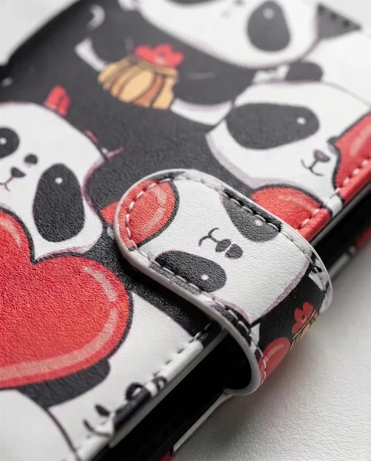 A wallet or purse with a panda design printed on it, featuring multiple panda faces and red hearts.