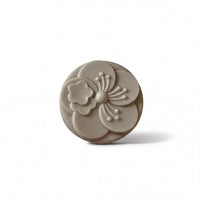 A gray, oval-shaped soap with a flower design on it.