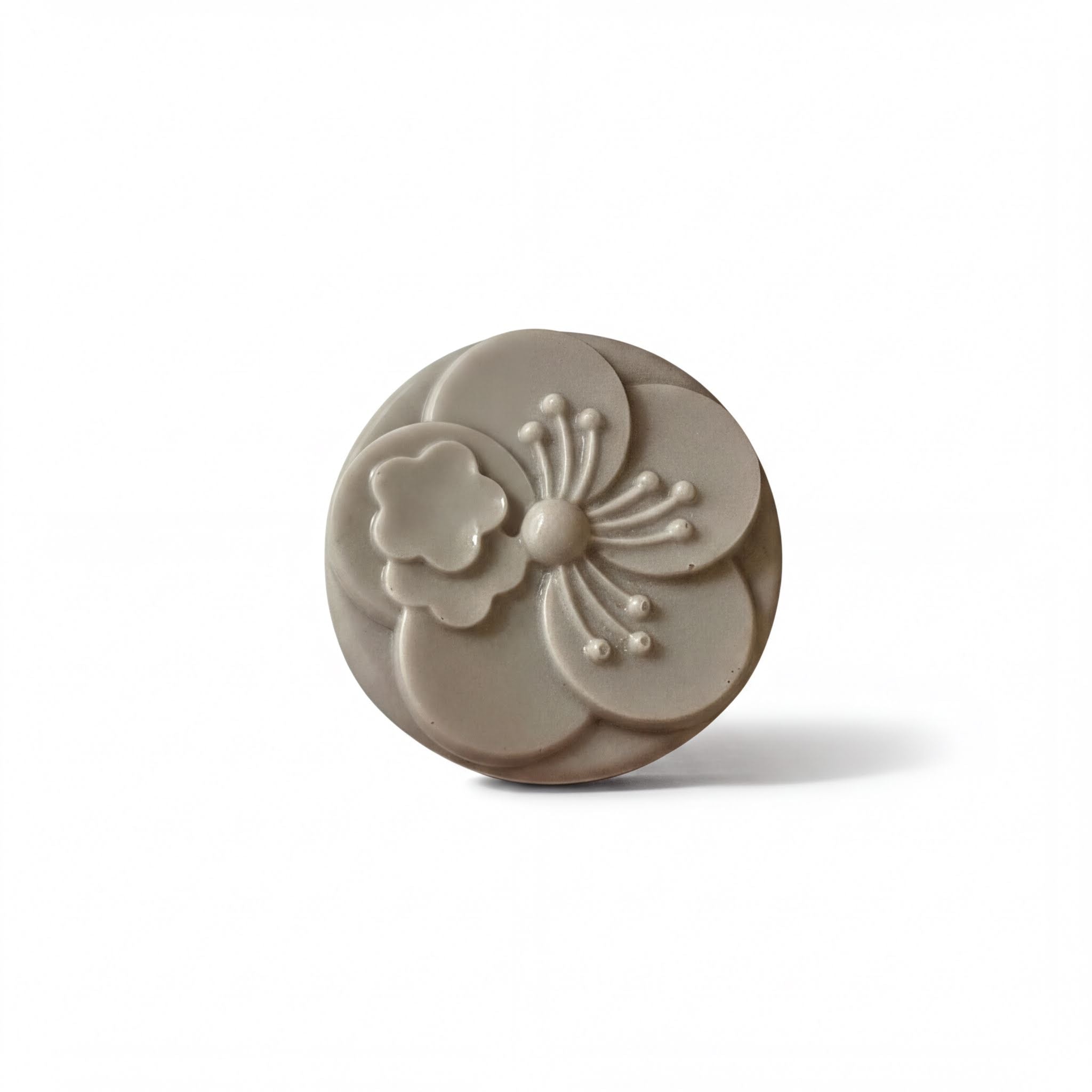 A gray, oval-shaped soap with a flower design on it.