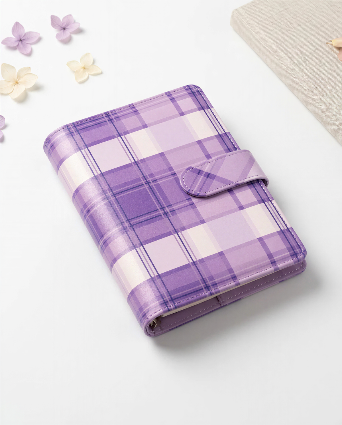 A purple and white plaid leather wallet or book cover is displayed on a white surface, surrounded by small purple flowers.