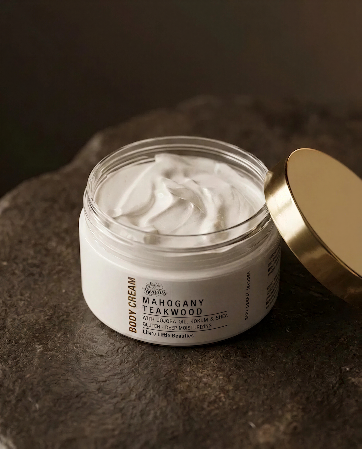 A jar of body cream with a gold lid, sitting on a dark surface.