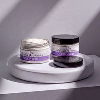 Two jars of lavender and vanilla body cream are placed on a white pedestal against a white wall, with sunlight casting shadows on the pedestal.