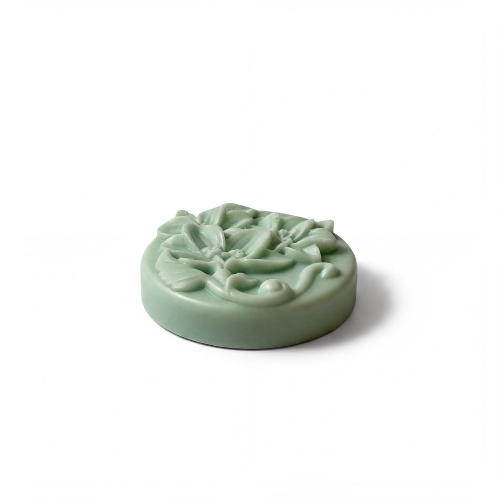 A round, green soap with a floral design on it.