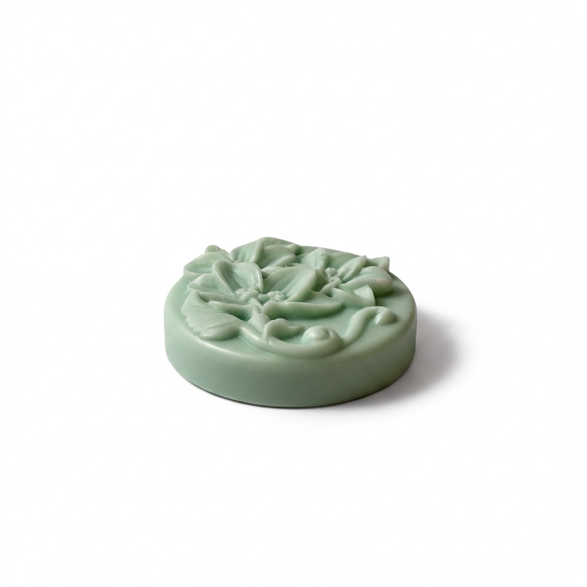 A round, green soap with a floral design on it.