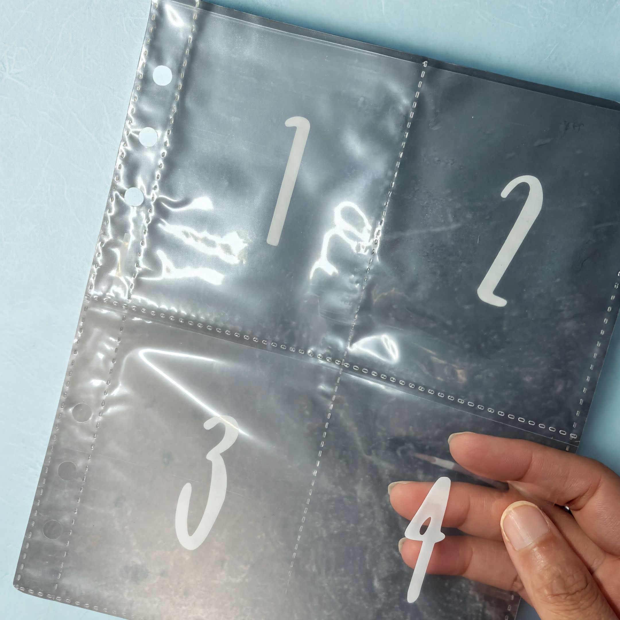 A hand is holding a transparent plastic page with numbers 3, 4, and 2 visible.