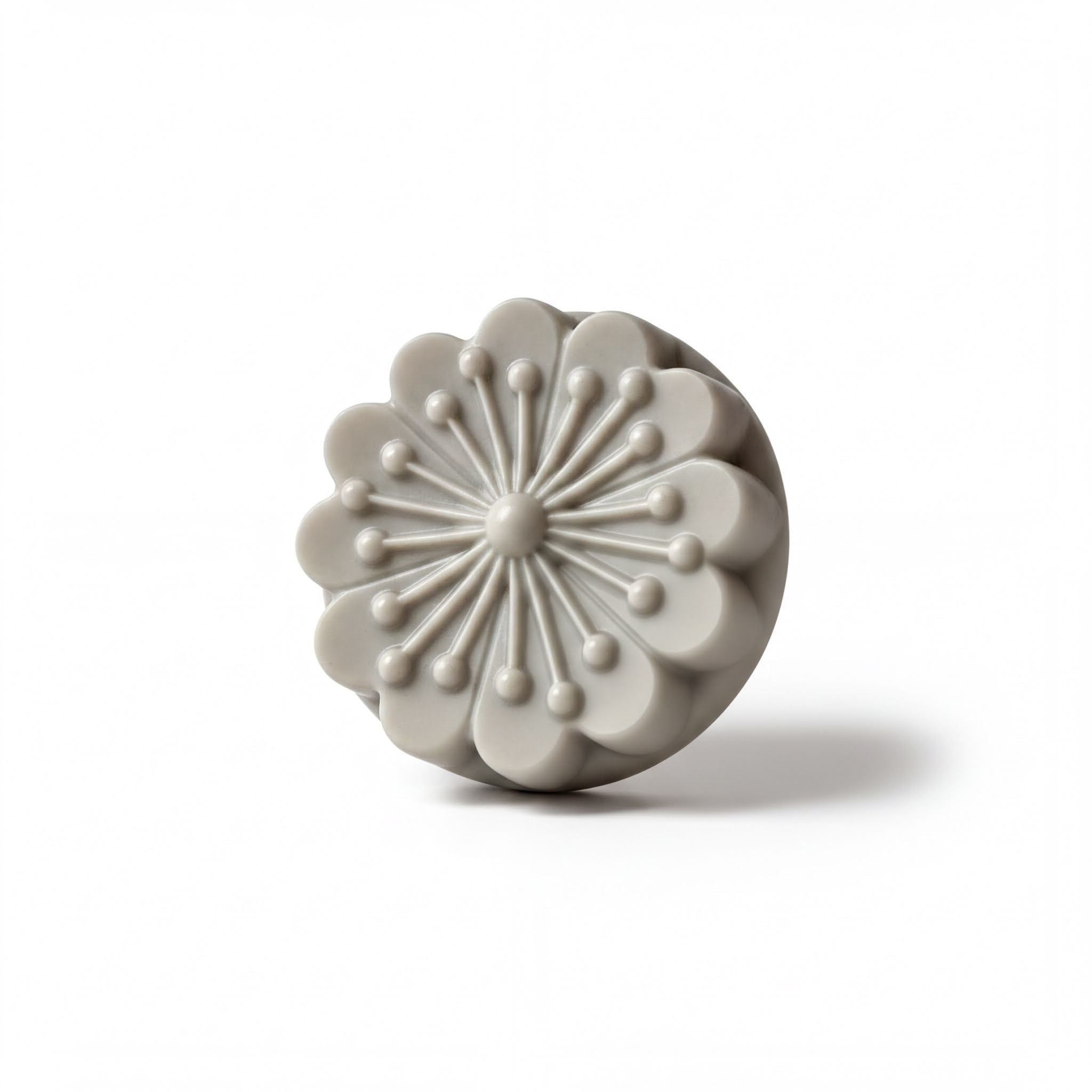 A gray, round soap dish with a flower-like design on it.