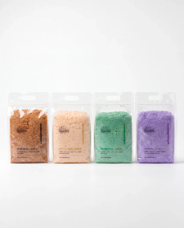four packages of bath salt, each with a different color and labeled with the brand name.