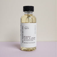A bottle of "Midnight Berry & Cream" body spray with a black cap, sitting on a light pink background.