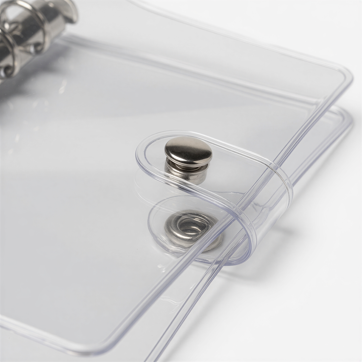 A transparent plastic binder with metal fasteners, including a top ring and a bottom ring, is shown in the image.