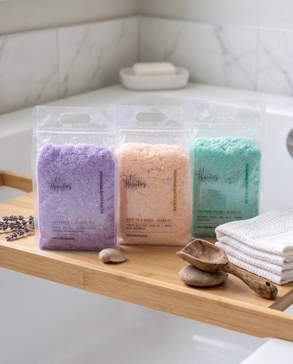 Three bags of bath salt from the brand "BeAUTIES" are displayed on a wooden shelf in a bathroom.