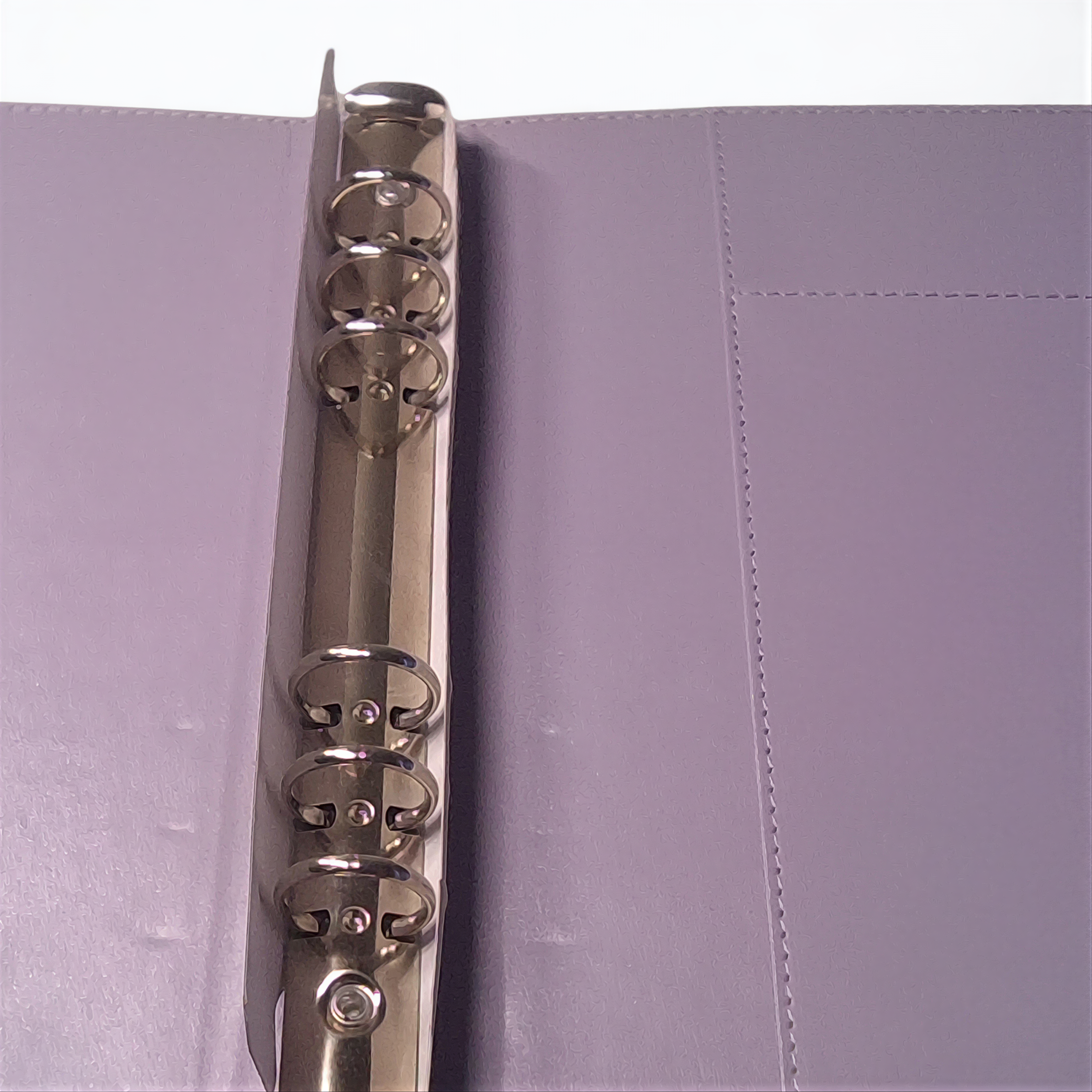 A silver metal ring is attached to a purple folder, with the ring's teeth visible.