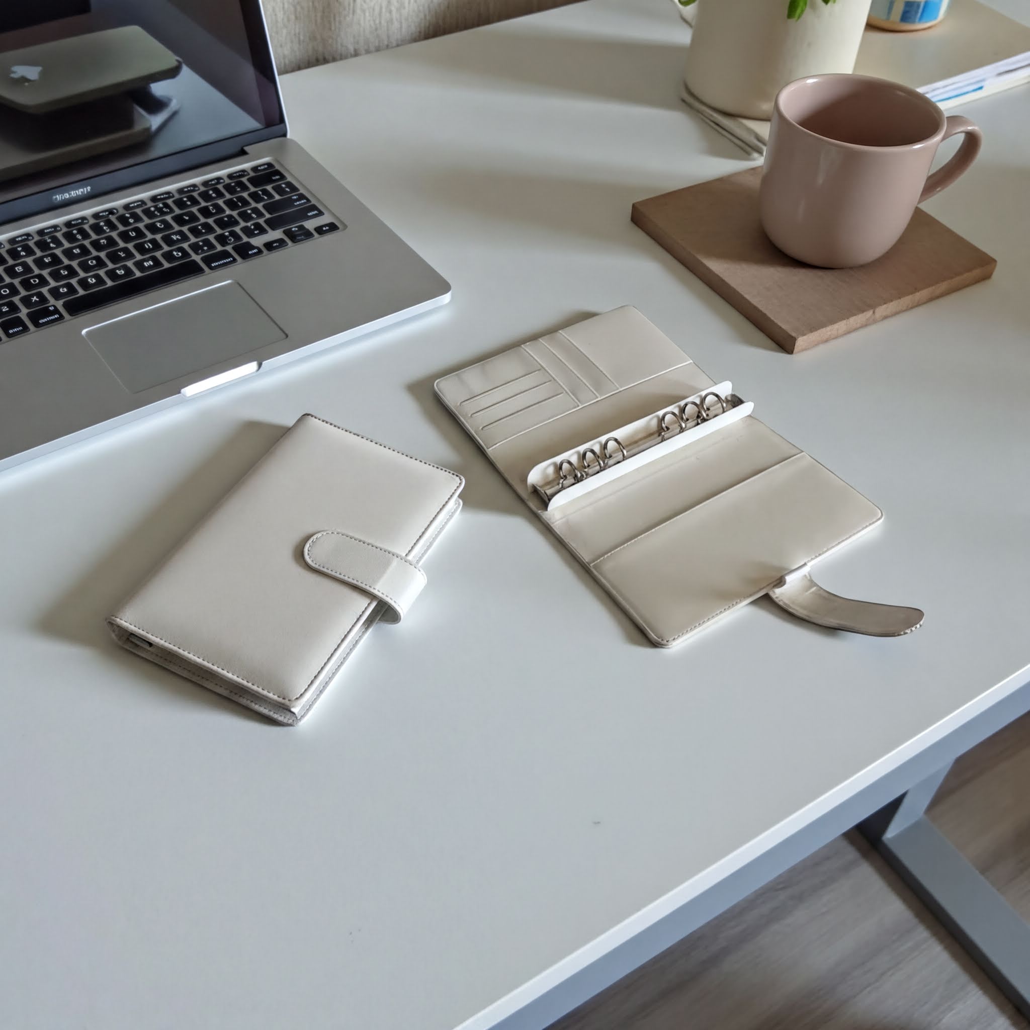 a white desk with a laptop, a wallet, a coffee cup, and a plant.