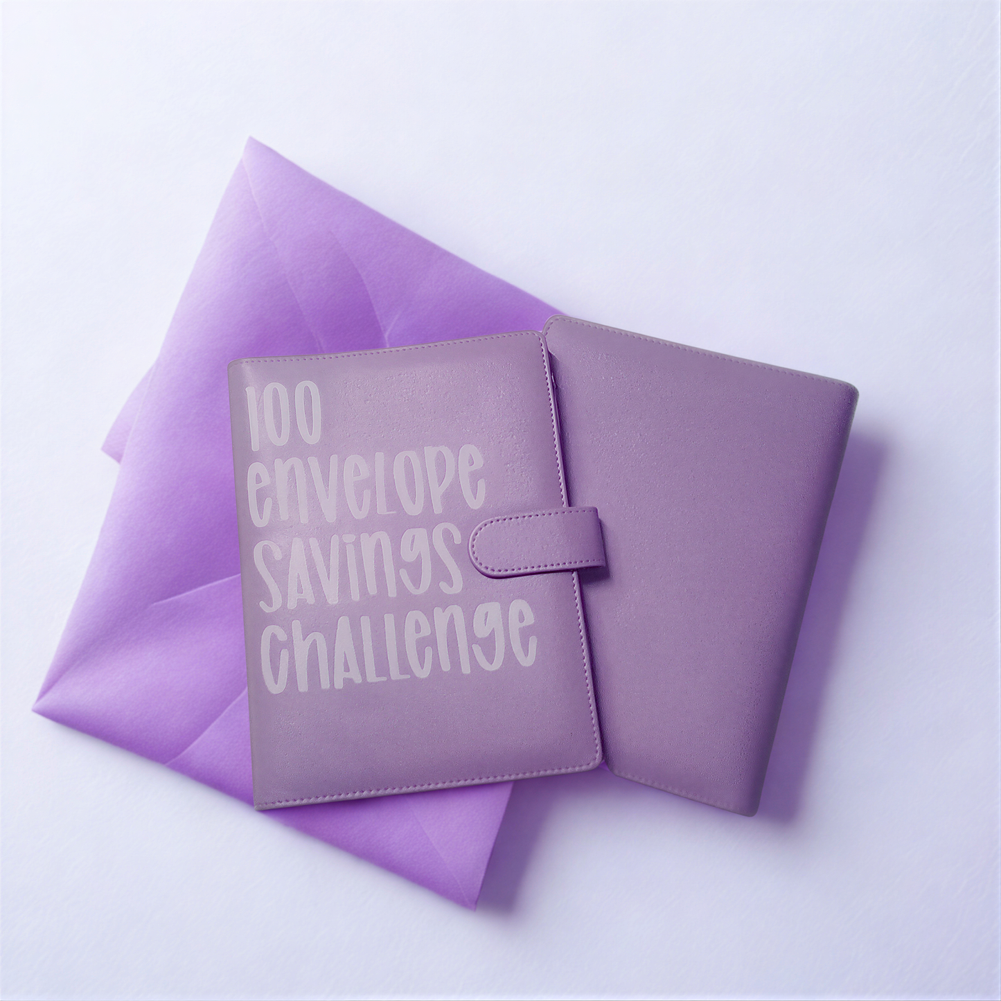 A purple folder or binder with the text "100 envelope savings challenge" printed on it, placed on top of a purple envelope.