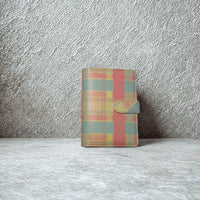 A colorful plaid wallet or book cover is displayed against a textured gray wall.